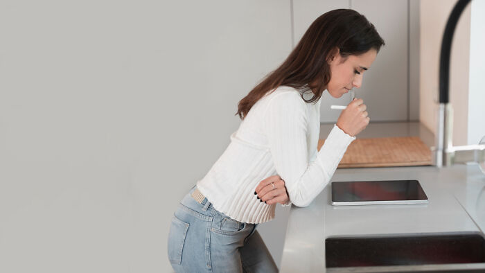 Woman leaning on kitchen counter looking unwell