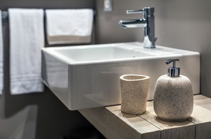 Bathroom sink with soap dispenser and cup on wooden countertop in modern bathroom