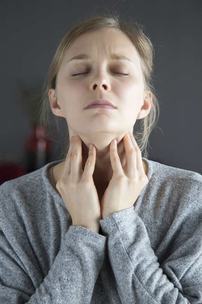 A woman with her eyes closed, touching her throat, experiencing extreme illness or sickness.