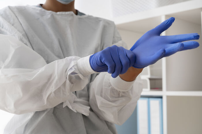 Person wearing blue protective gloves and medical gown