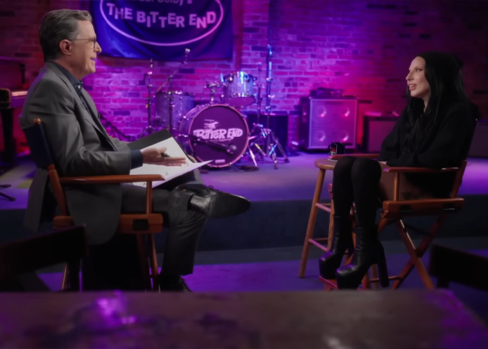 Lady Gaga expecting first baby. She wears a black top, with high heel boots, sitting with Stephen Colbert.
