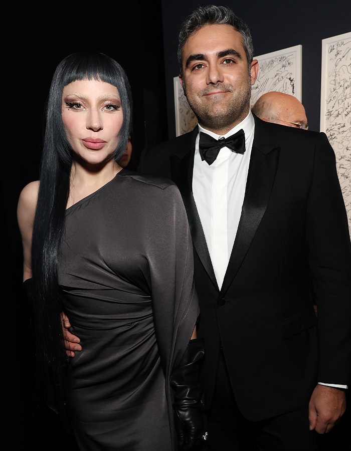 Lady Gaga expecting first baby. She wears a black one-shoulder dress, with a man in a black suit.