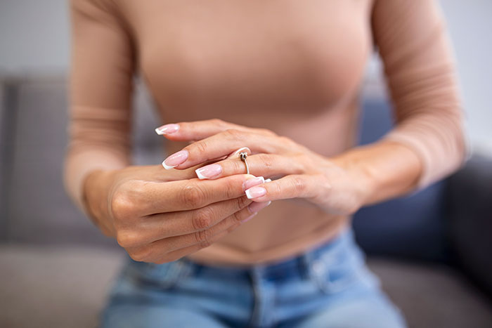 A woman struggles to remove a sapphire engagement ring from her finger.