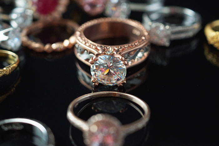 A close-up of a sapphire engagement ring surrounded by other rings on a reflective surface.