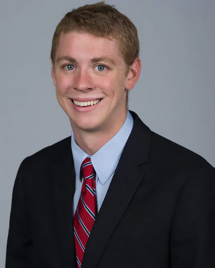 Brock Turner smiling in a suit and red patterned tie for a headshot. Brock Turner smiling in a suit and red patterned tie for a headshot.