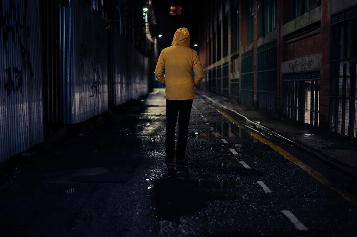 A person in a yellow jacket walks down a dark alley in a small town, a setting for unsettling stories.
