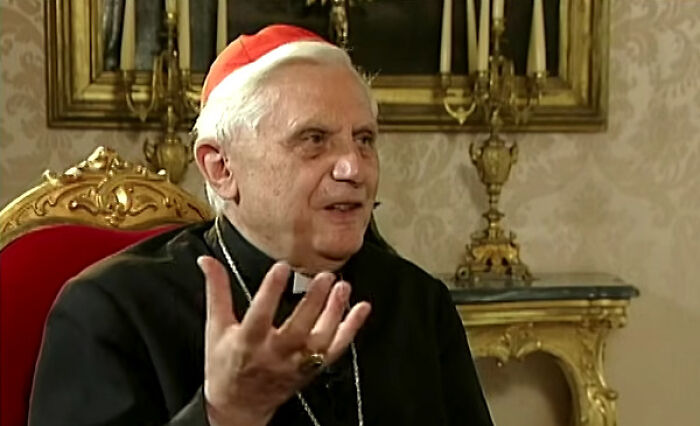 An older man in religious attire, possibly a cardinal, gesturing while speaking, suggesting unsettling stories from his past.