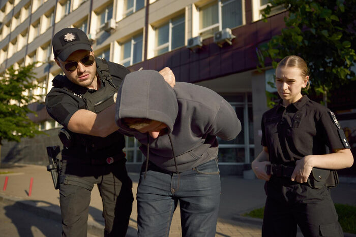 Police officers arresting a person in a hooded sweatshirt on a sunny day. Unsettling stories from small towns.