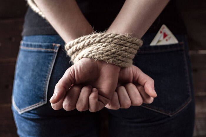A person with their hands tied behind their back, suggesting unsettling stories and shocking secrets from small towns.