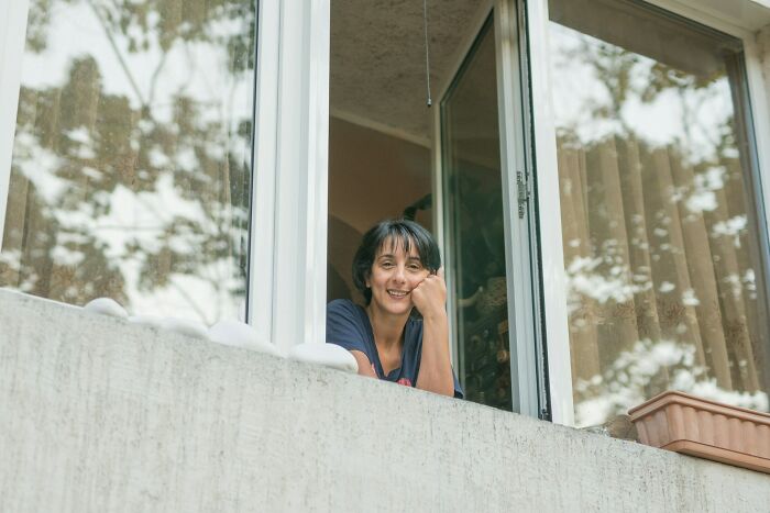 A smiling woman looking out from a window, symbolizing the quiet places where shocking secrets may reside in small towns.