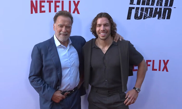 Arnold Schwarzenegger and another man at a premiere, a celebrity event that contrasts with unsettling stories from small towns.