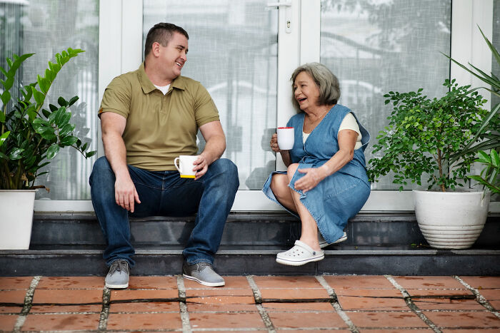 A man and an older woman sitting on steps, enjoying a conversation, a common sight in small towns that might hold shocking secrets.