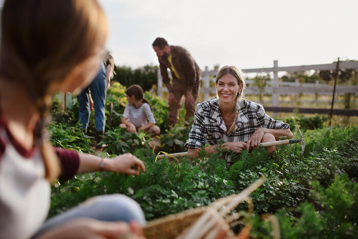 A woman smiling while gardening, with other people in the background. Unsettling stories from small towns reveal hidden secrets.