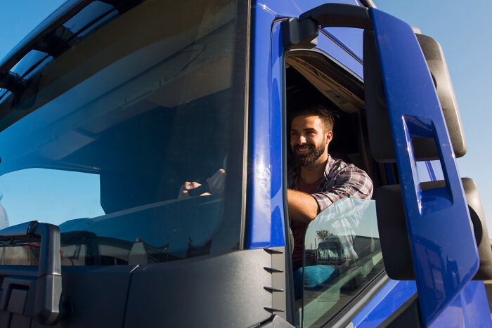 A man smiling while sitting in the driver's seat of a blue truck. This image tells unsettling stories from small towns.