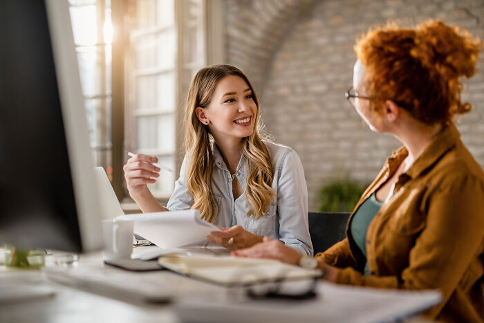 Two female colleagues talking in an office, discussing career and marriage regrets