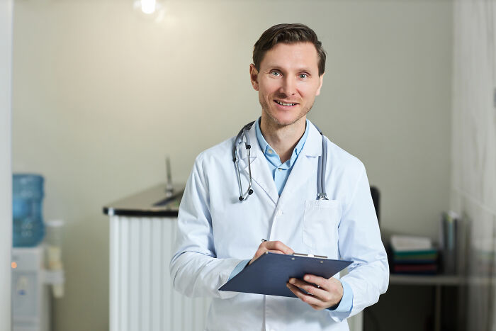 A male doctor in a white coat holding a clipboard, symbolizing healthcare experiences and subtle sexism