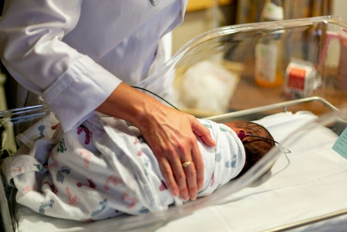 A person tending to a swaddled baby in an incubator, illustrating the origins of a parent-child relationship.