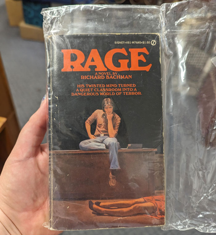 A hand holding a copy of Stephen King's pulled book Rage by Richard Bachman, in plastic. A hand holding a copy of Stephen King's pulled book Rage by Richard Bachman, in plastic.