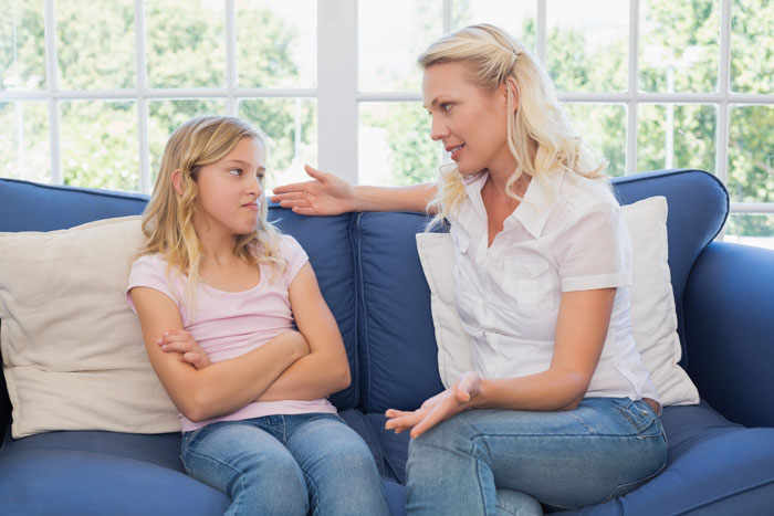 A woman talks with her adult stepdaughter on a blue couch, discussing family problems or insults. A woman talks with her adult stepdaughter on a blue couch, discussing family problems or insults.
