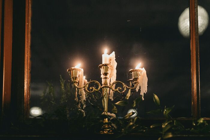 A gold candelabra with melting wax candles against a dark window, perfect for moody weddings