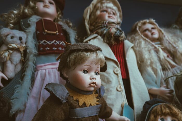A collection of weird, antique dolls with porcelain faces and elaborate clothing at someone's home.