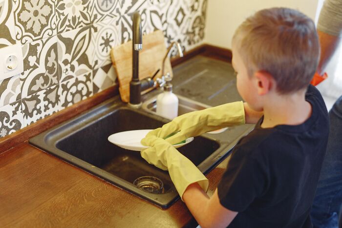 Child washing dishes wearing yellow gloves in home kitchen