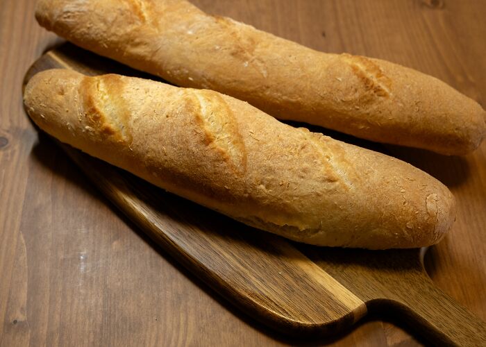 Two baguettes on a wooden cutting board, representing weird things people were not prepared to see at someone's home.