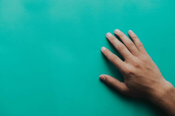 A hand resting on a green surface, illustrating weird things people were not prepared to see at someone's home.