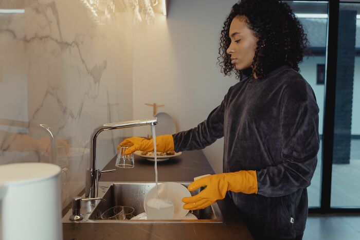 A person in yellow gloves washing dishes in a modern kitchen sink, showing unexpected weird things at home.