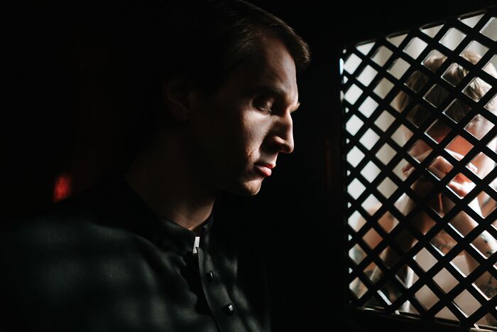 A weird confessional, priest listening intently, suggesting things not prepared to see at someone's home.