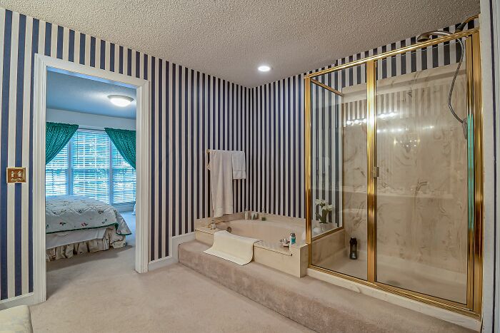 A weird bathroom with striped wallpaper, a large tub, and a gold-framed shower. Things not prepared to see at home.