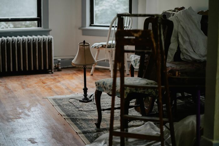 A weird and messy living room with old chairs, a lamp, and a radiator. Things not prepared to see at someone's home.