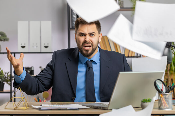 An angry businessman sitting at a desk with flying papers, illustrating satisfying stories.