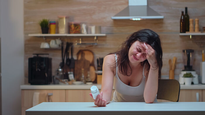A young woman with a headache holding a pill bottle, brushing off sepsis symptoms as a bad hangover.