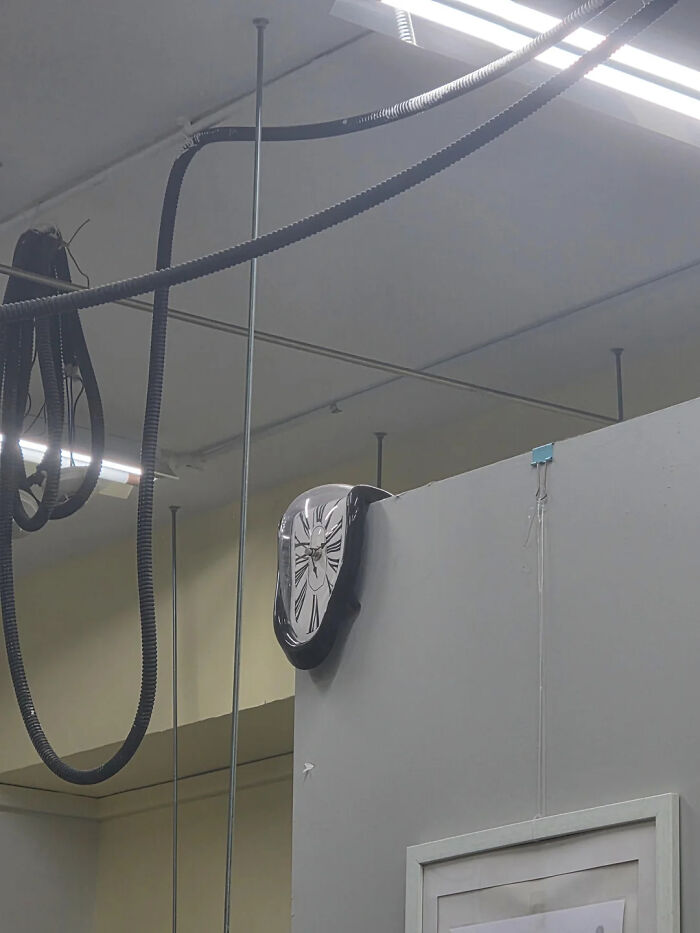 Hilarious photos: A melting clock hanging over the edge of a wall in a room with exposed ceiling pipes.