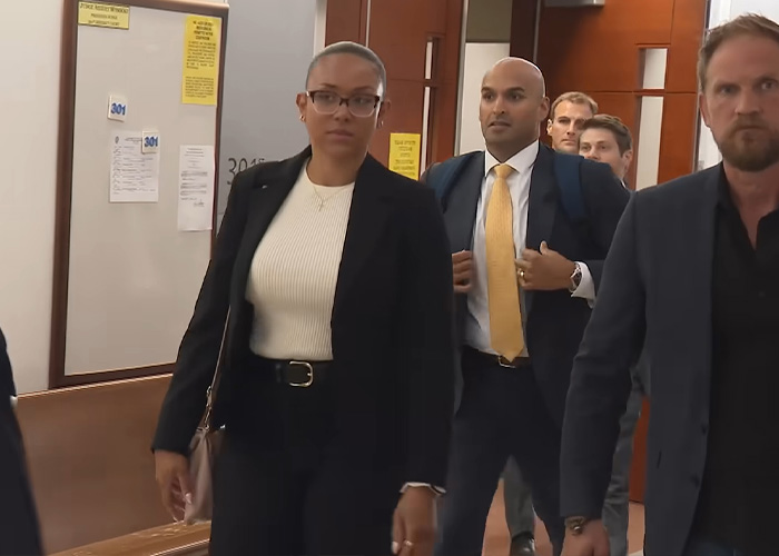 A group of people, including a woman with short hair and a man in a yellow tie, walking in a hallway, related to the surrogate who refused to end the pregnancy. A group of people, including a woman with short hair and a man in a yellow tie, walking in a hallway, related to the surrogate who refused to end the pregnancy.