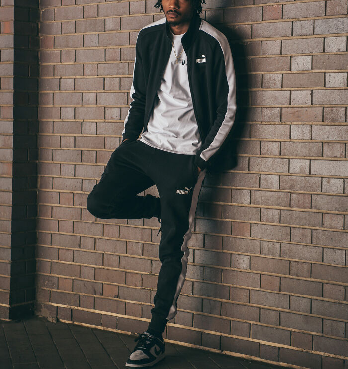 Man in a tracksuit leaning against a brick wall, perhaps waiting for or after an awkward first date.