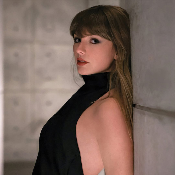 Taylor Swift leaning against a wall in a sleek, high-neck sleeveless black dress looking at the camera Taylor Swift leaning against a wall in a sleek, high-neck sleeveless black dress looking at the camera