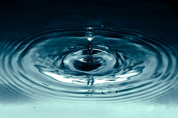 A single water droplet creating ripples on a dark blue surface, illustrating cool facts about the universe's physics.