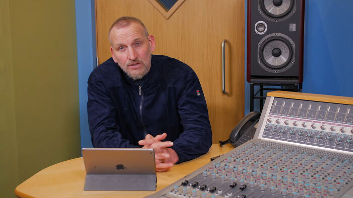 A man sitting in a recording studio next to a mixing console, representing new facts about the music industry