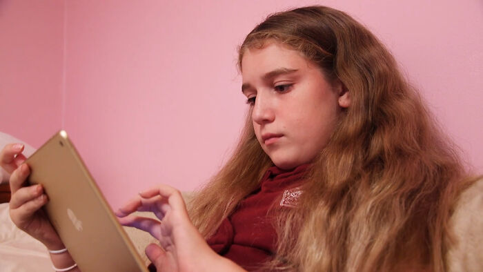 A young girl with long hair looking at a digital tablet, sharing new facts about online learning