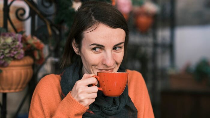A smiling woman sipping from an orange mug, illustrating new facts people learned