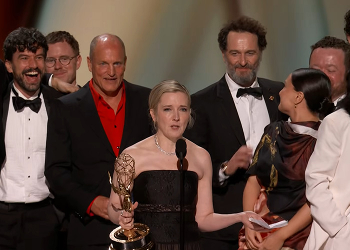 An Emmy winner speaks at the podium, surrounded by her castmates at the Emmy Awards. An Emmy winner speaks at the podium, surrounded by her castmates at the Emmy Awards.