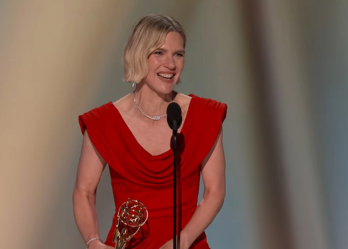 A smiling Emmy winner in a red dress holds her Emmy award while giving a speech at the Emmys. A smiling Emmy winner in a red dress holds her Emmy award while giving a speech at the Emmys.