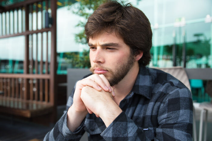 A close-up of a thoughtful man sitting outside, with hands clasped under his chin