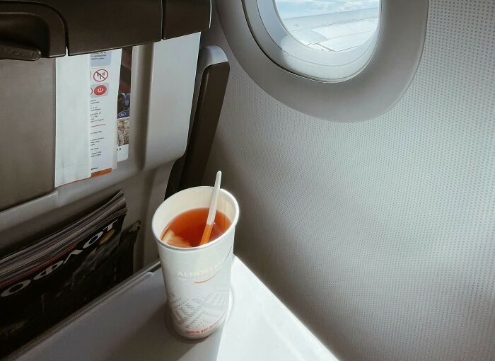 A beverage cup sitting on a plane seat table next to a window