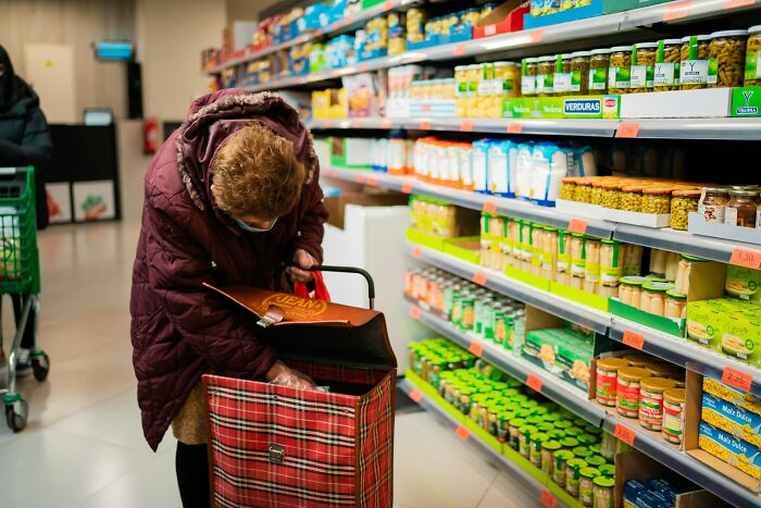 An older woman with a shopping cart in a grocery aisle, an activity people judge others for.