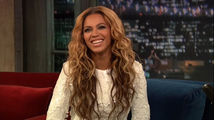 Singer Beyonce smiling with curly hair during a talk show, featured in celebrity encounters
