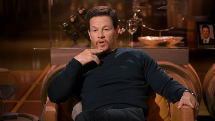 Mark Wahlberg sitting in a chair holding his chin during a celebrity encounter interview