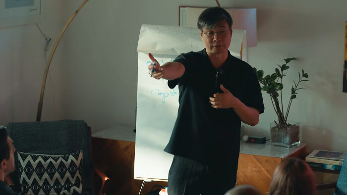 Chinese Nostradamus gesturing while presenting predictions for 2027 to a group.